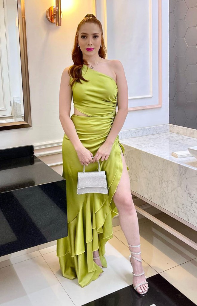 Adriana García in a light green one-shoulder dress with a ruffled skirt and a small silver handbag.