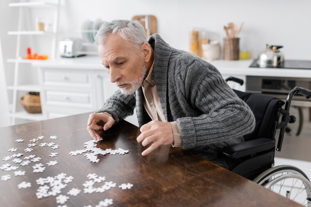 Man with Parkinson's syndrome sitting in a wheelchair and doing a jigsaw puzzle.