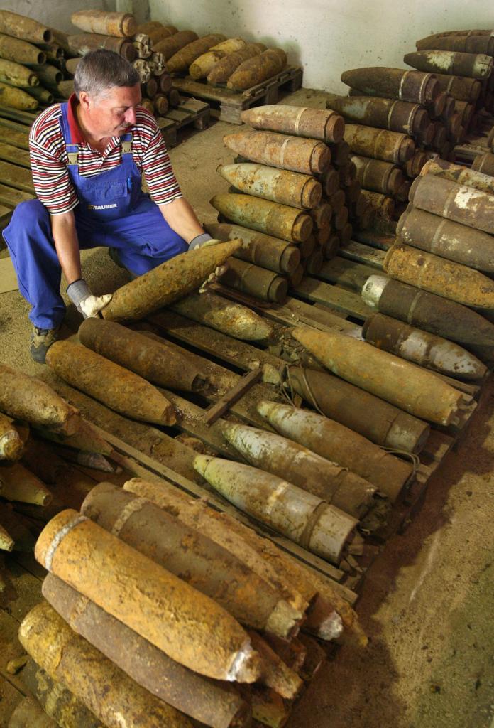 Man handling a rusted World War II aircraft bomb among piles of other munitions.