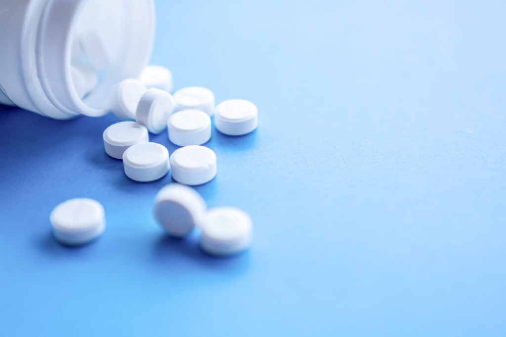 White pills spilling from a bottle onto a blue background.