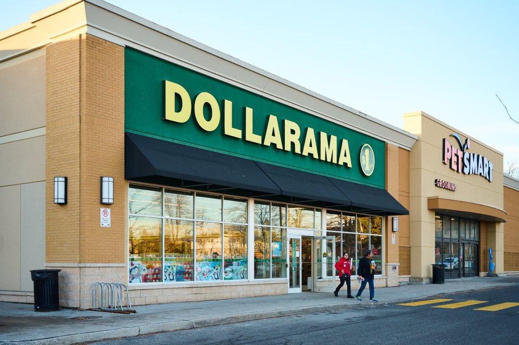 A Dollarama store with a green and yellow sign next to a PetSmart store, with two people walking in front.