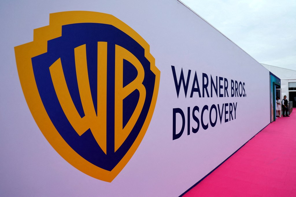 The Warner Bros Discovery logo is displayed on a large white sign with a pink carpet leading to a building.