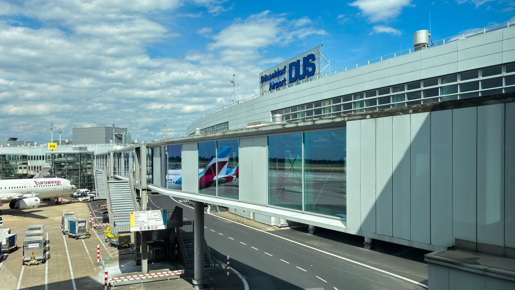 Düsseldorf Airport terminal building with the "Düsseldorf DUS Airport" logo on top and a Eurowings airplane at a gate.