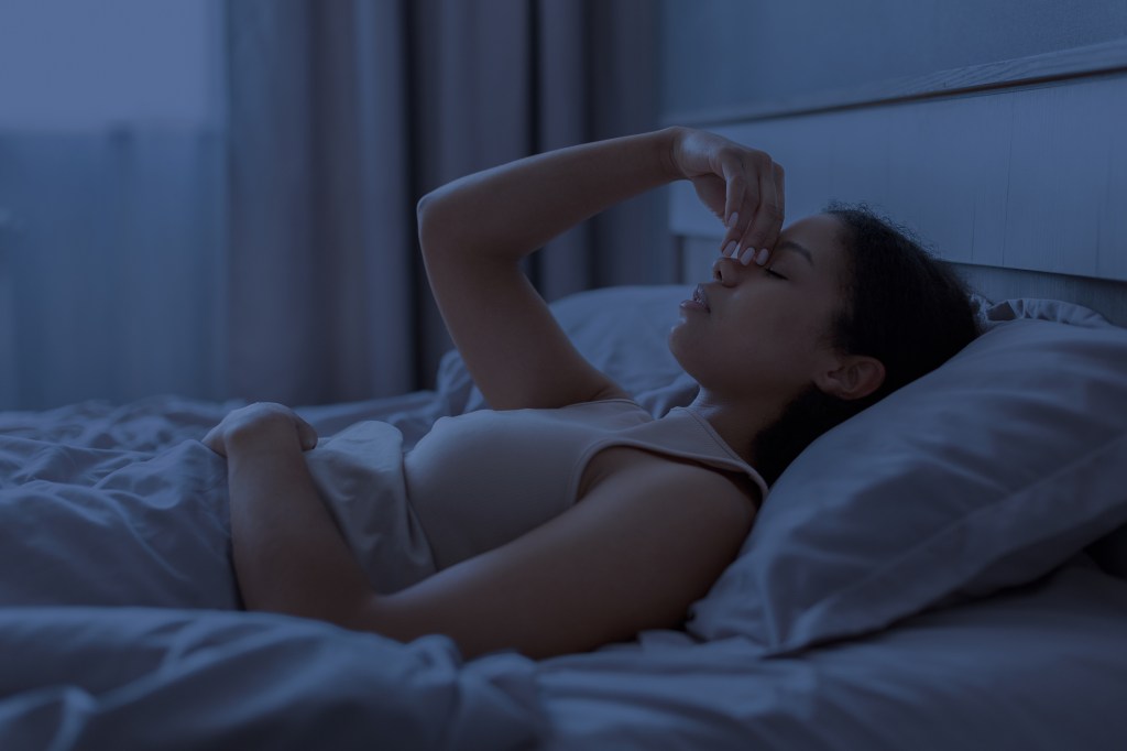 A woman lies awake in bed at night, pinching her nose as if experiencing sinus pressure or headache.