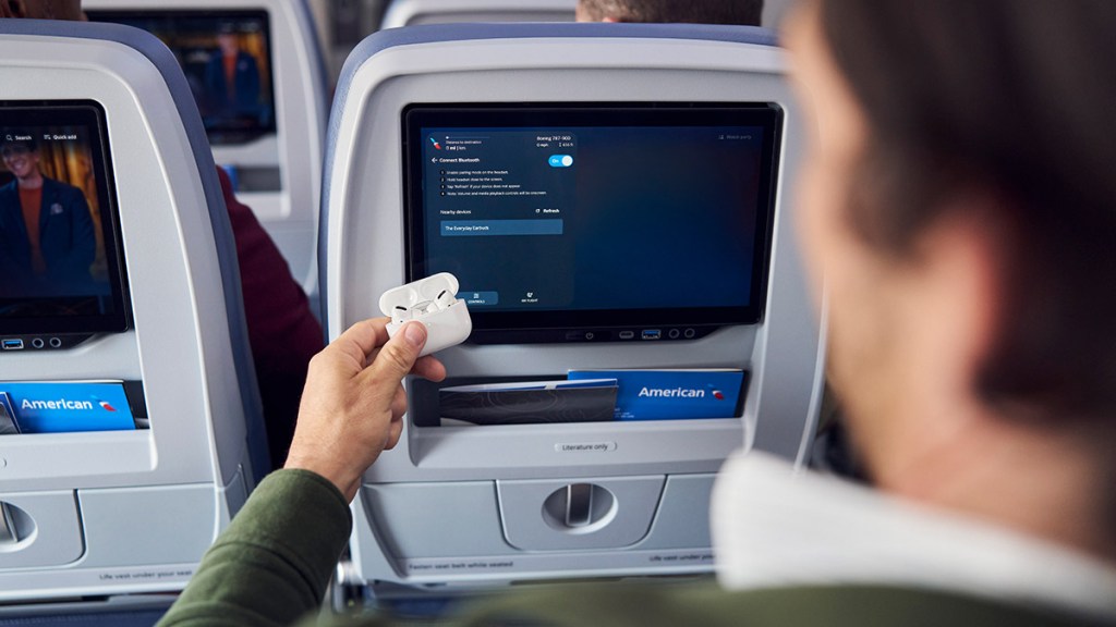 A person connects their Bluetooth earbuds to an American Airlines seatback entertainment screen.
