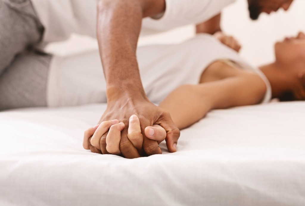 Close-up of an African couple holding hands in bed.