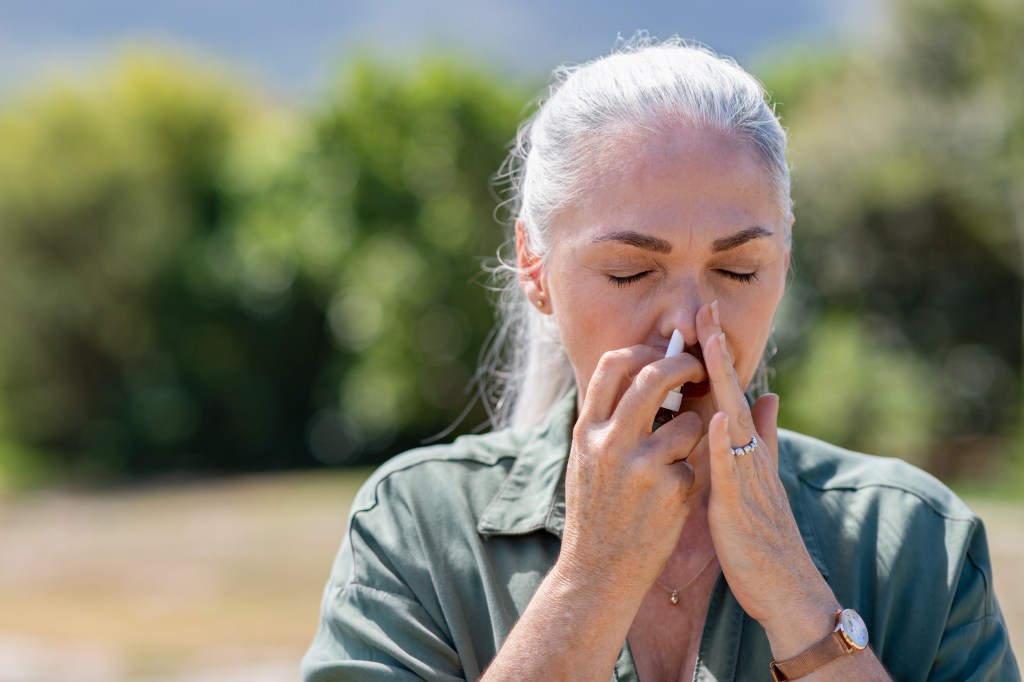 Senior woman using nasal spray for allergy.
