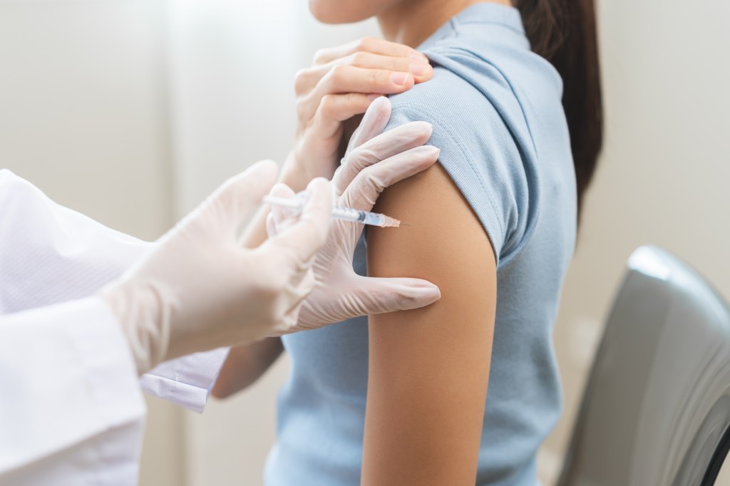 A gloved hand administering a vaccine shot to a patient's arm.