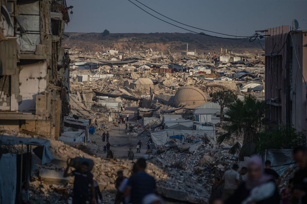 Palestinians navigate through a destroyed, rubble-filled Jabaliya with makeshift tents and damaged buildings.