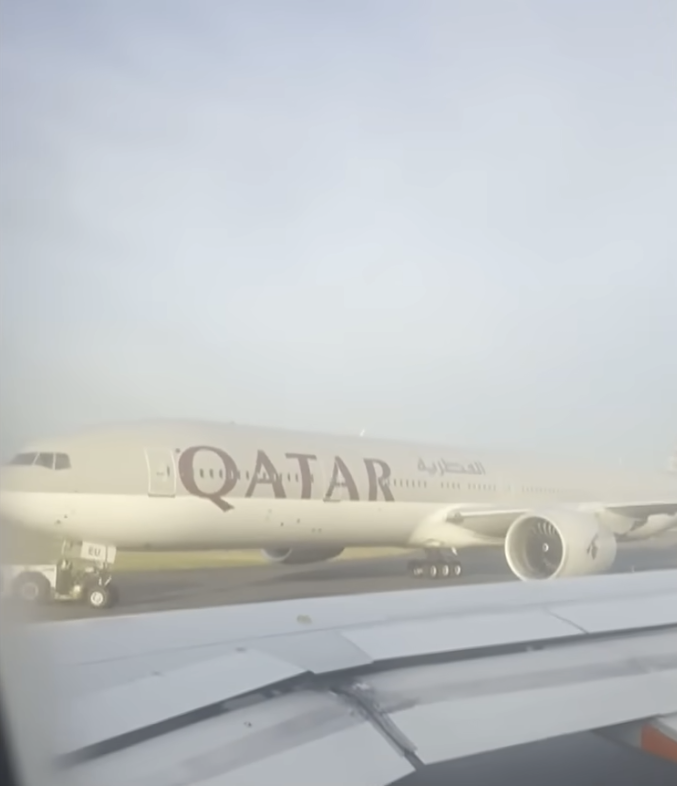 View from an airplane window of a Qatar Airways plane being towed.