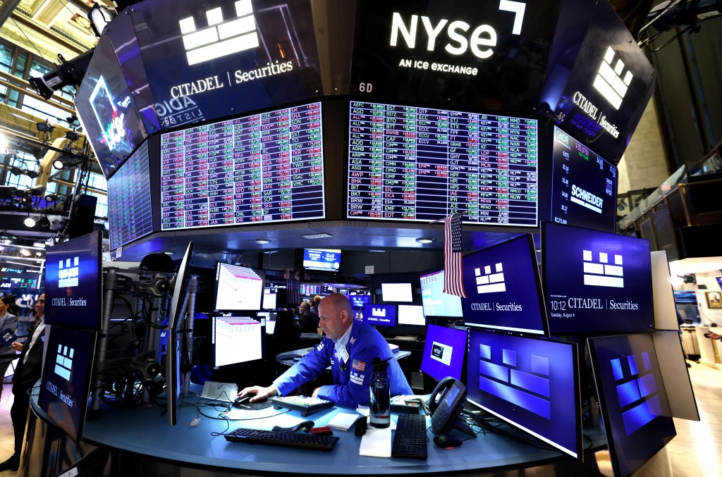A trader working at a desk surrounded by large screens displaying market data on the New York Stock Exchange floor.