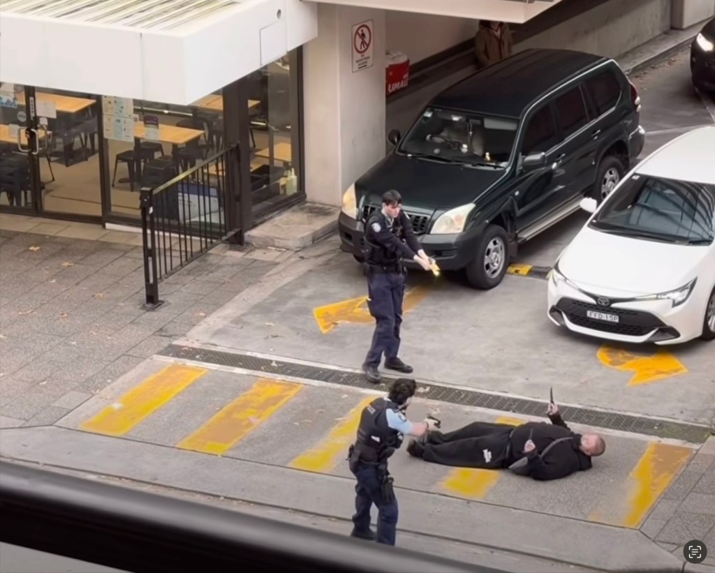 Two police officers with guns drawn apprehending a man lying on the ground holding two knives.