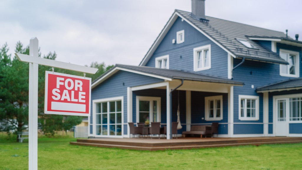 A red "FOR SALE" sign on a white post in front of a blue house with white trim.