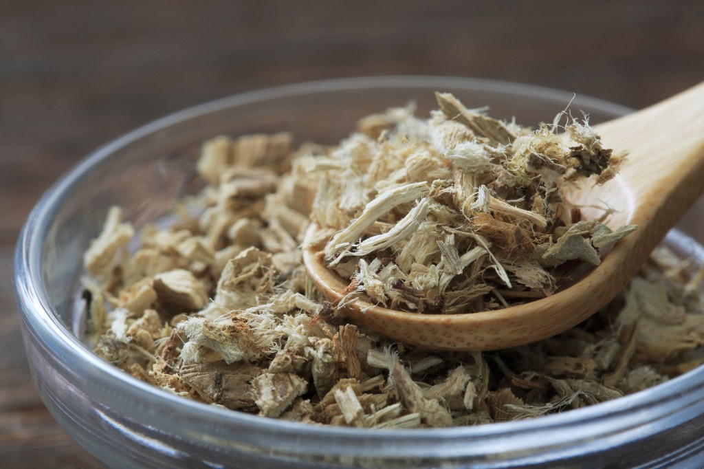 Close-up of dried marshmallow root pieces in a glass bowl, with some on a wooden spoon.