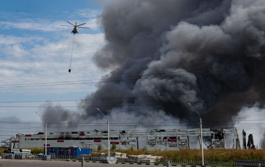 A firefighting helicopter flies above a burning Wildberries facility.