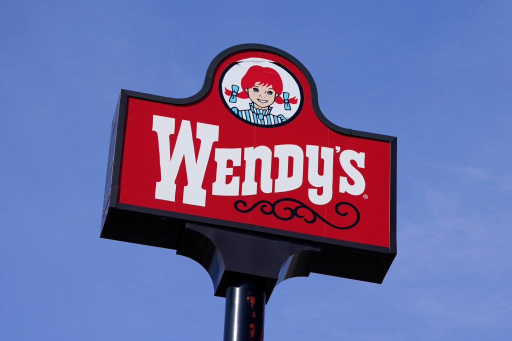 A Wendy's restaurant sign against a clear blue sky.