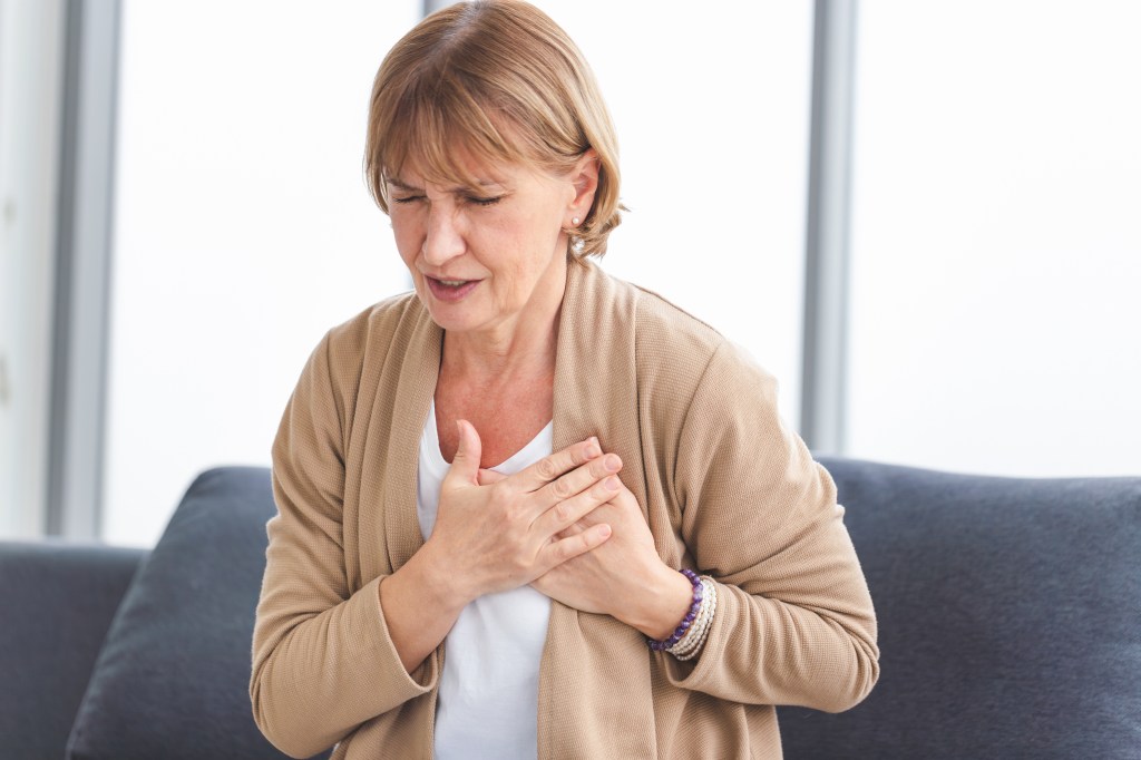 Mature woman clutching her chest in pain, likely from a heart attack.
