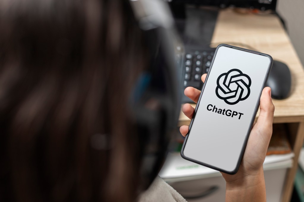 A teen holding a mobile phone displaying the ChatGPT logo.