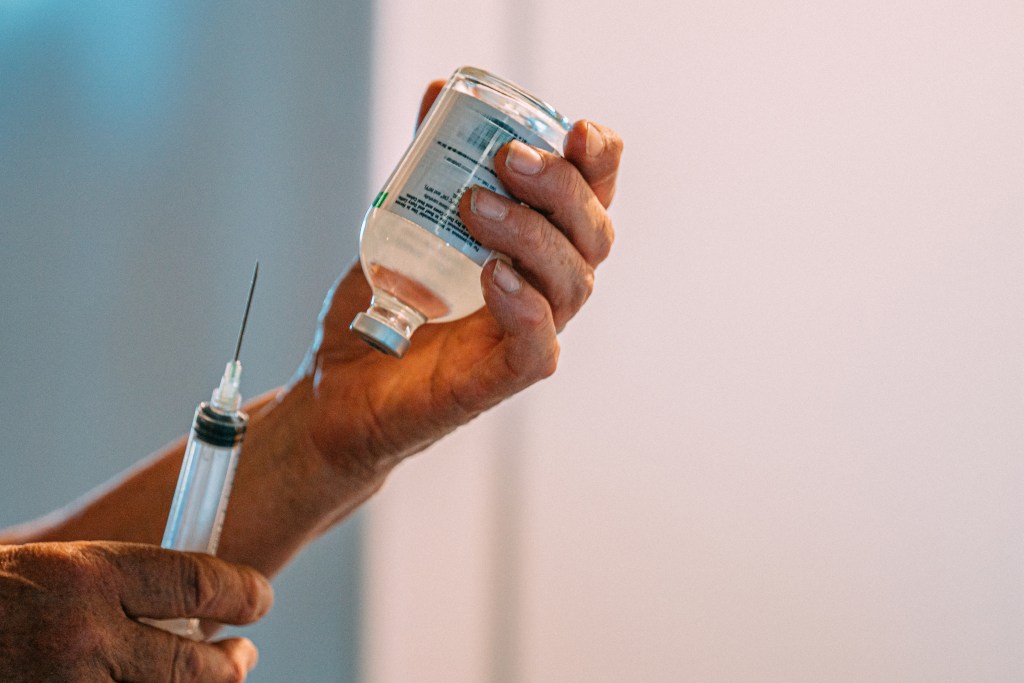 A veterinarian draws medication from a glass vial with a syringe.