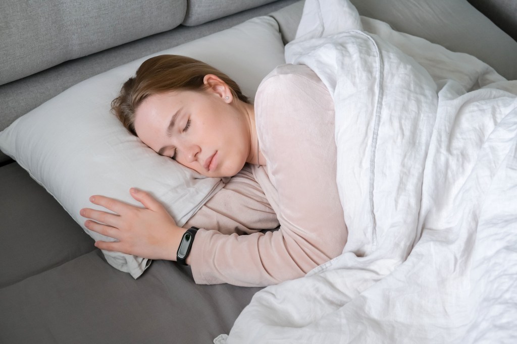 Woman sleeping in bed, wearing a fitness tracker to optimize circadian rhythm and fight insomnia.