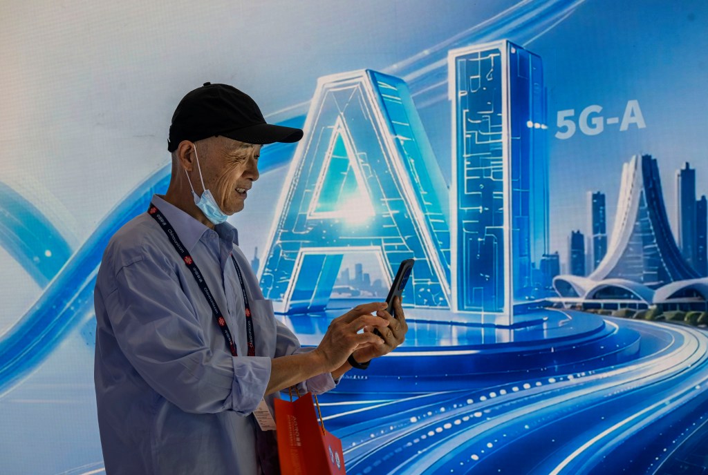 A man uses a mobile phone in front of a screen displaying "AI" and "5G-A" at a telecom expo.