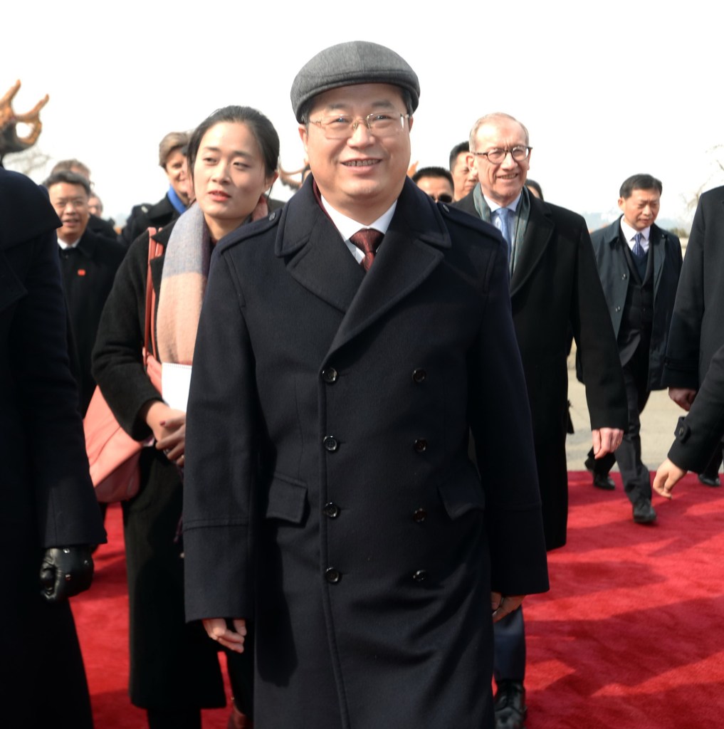 Chen Yixin, Communist Party boss of Wuhan, stands smiling on a red carpet while wearing a dark coat and cap.