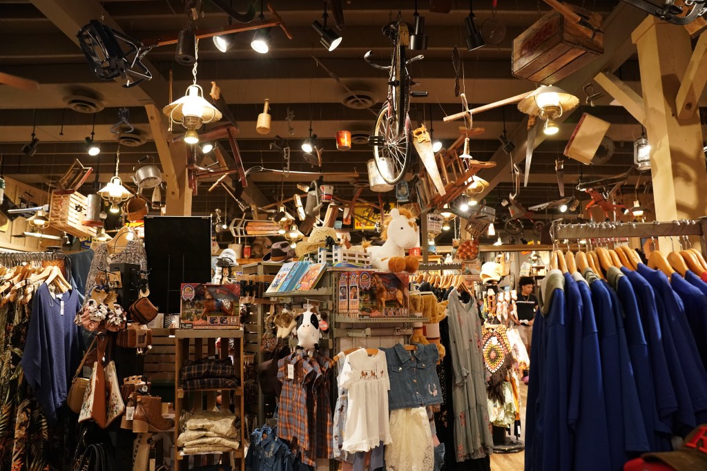 The interior of a Cracker Barrel Old Country Store, with clothing racks, various items for sale, and antiques hanging from the ceiling.