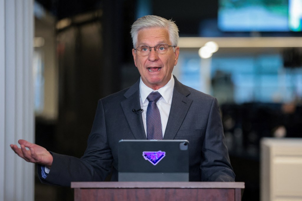 Federal Reserve Board Governor Christopher Waller speaking at a podium with a tablet.