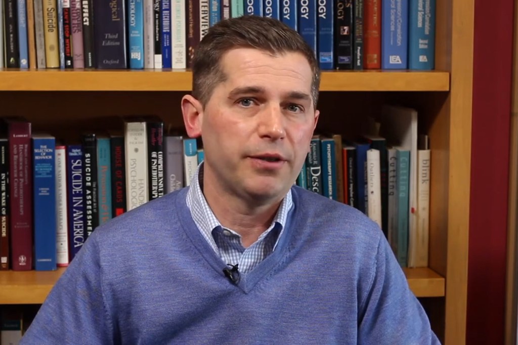 Psychologist Matthew Nock in front of a bookshelf filled with books about psychology, suicide, and self-injury.
