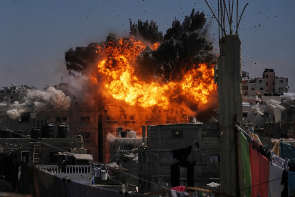 An explosion of fire and smoke erupts behind buildings in Gaza City following an Israeli airstrike.