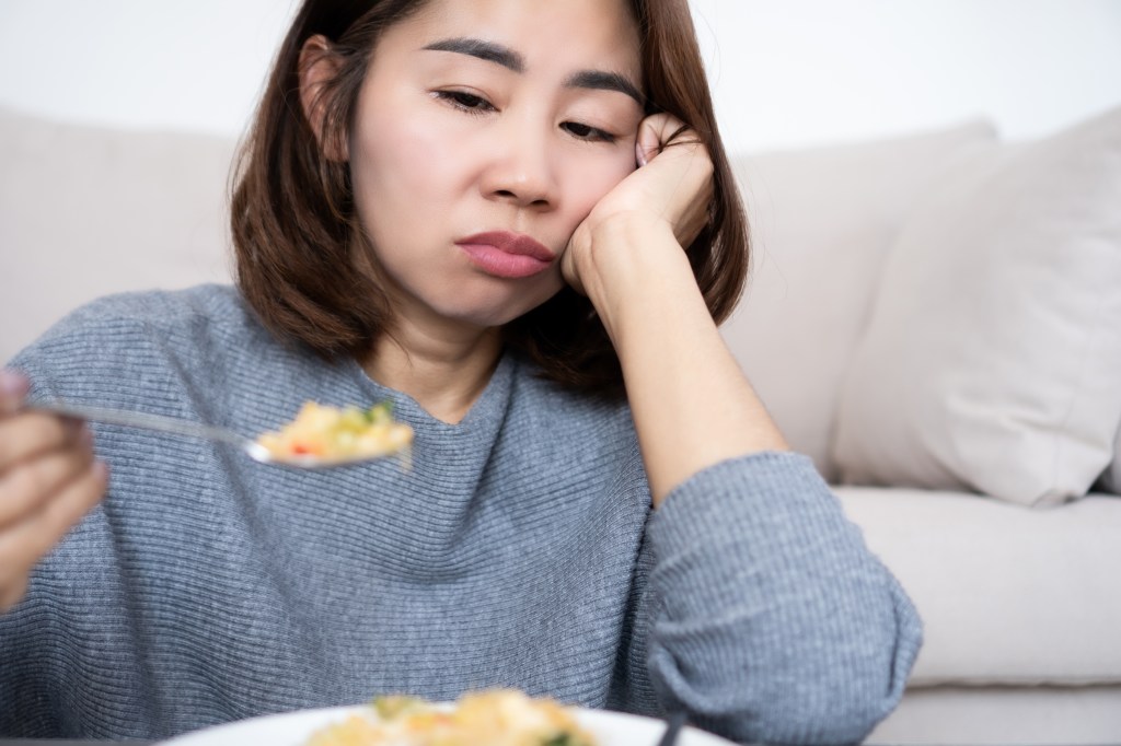 A woman looking bored and unhappy while holding a spoon of food