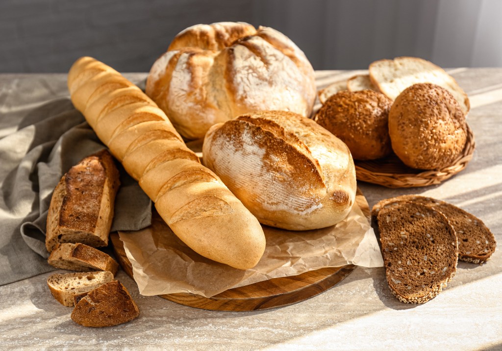 An assortment of freshly baked bread, including baguettes, round loaves, and sliced rye bread, on a table.