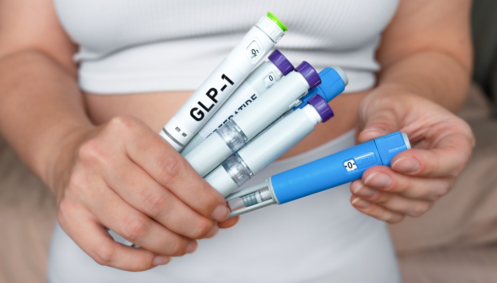 A woman holds several GLP-1 and Tirzepatide injection pens for weight loss and diabetes treatment.