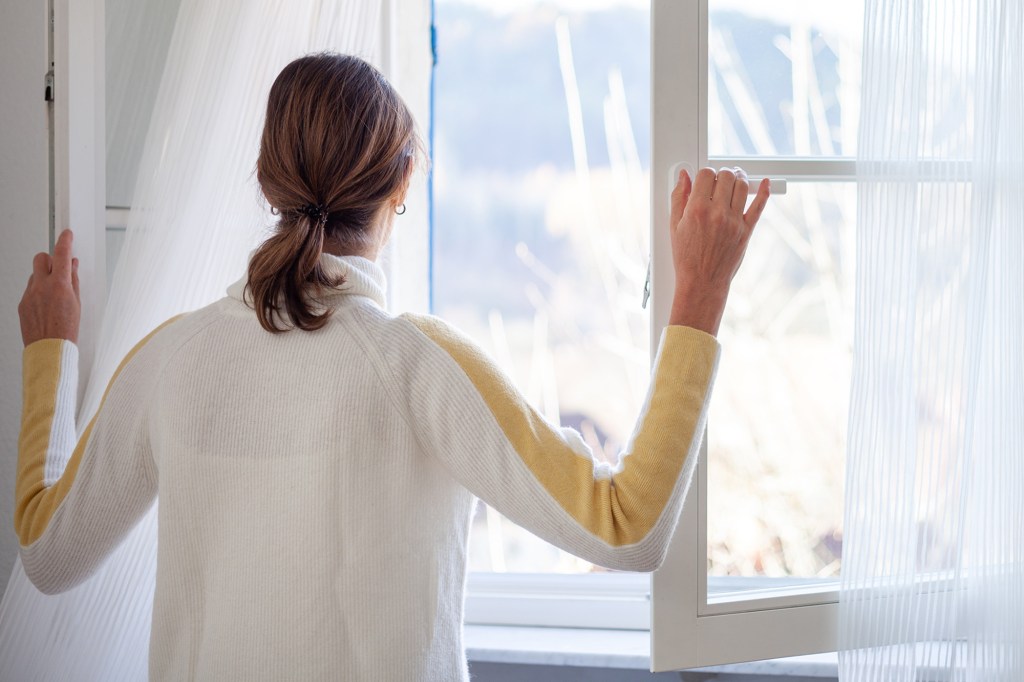 A woman in a white sweater with yellow stripes opening a window.