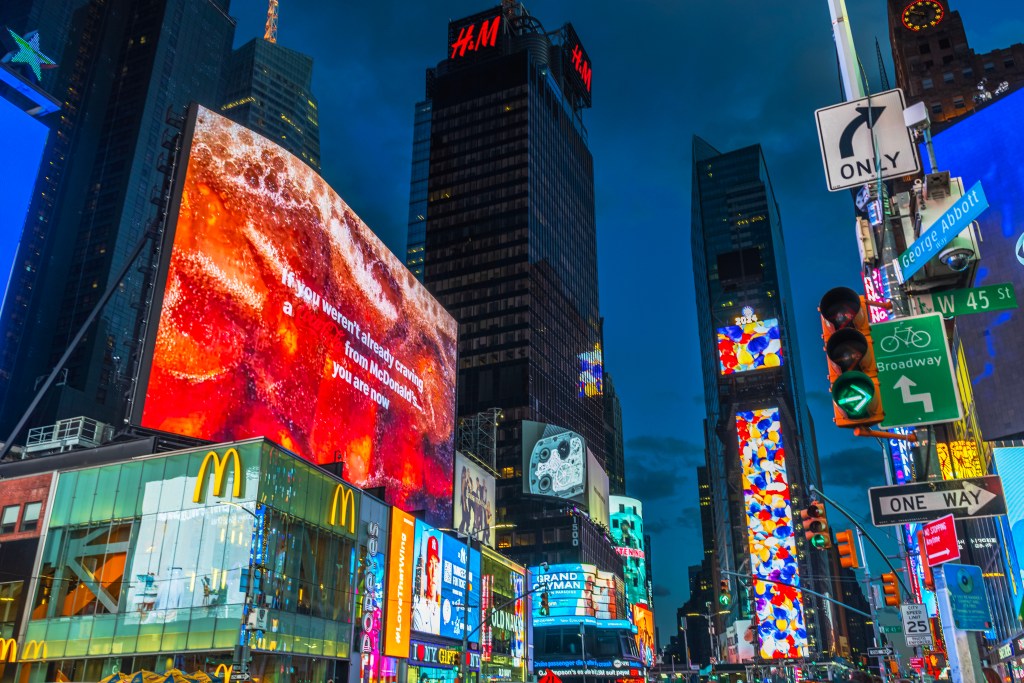 Times Square at night, with towering buildings illuminated by vibrant digital billboards advertising McDonald's and H&M.