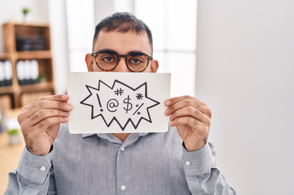 Man holding a sign with symbols of swear words.