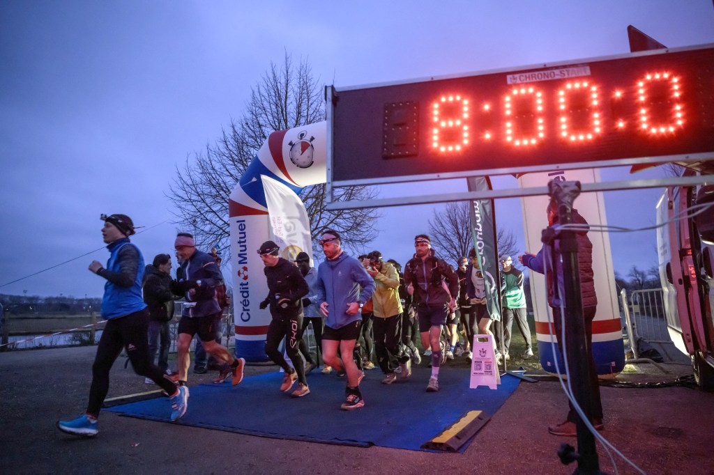 Competitors start a loop during an ultra-endurance backyard race under an illuminated digital clock.