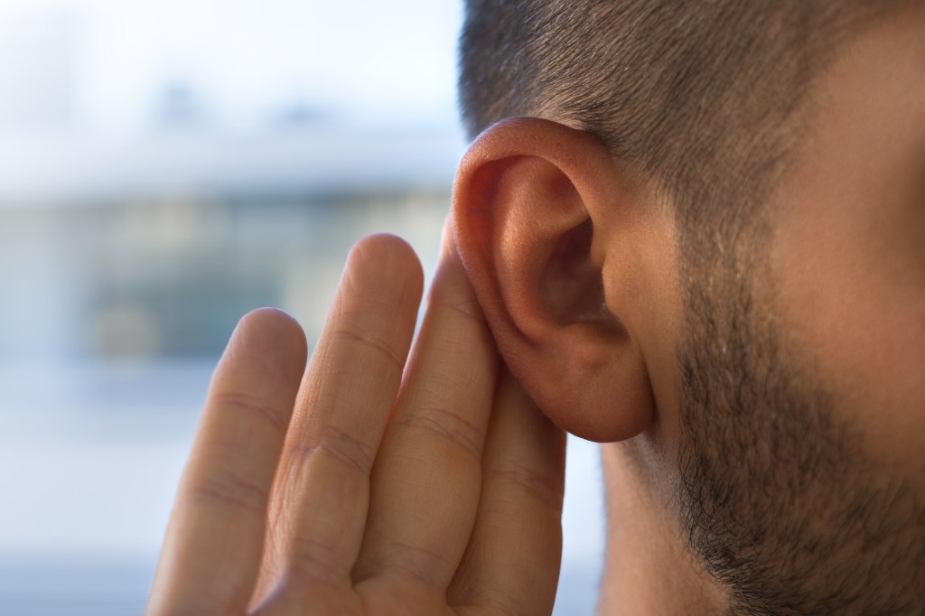 A young man cupping his hand to his ear to listen.
