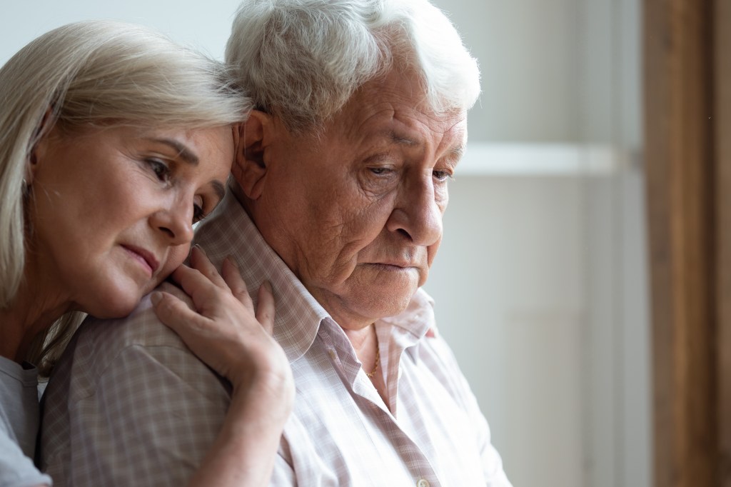 Middle-aged daughter comforts her elderly father by embracing him.