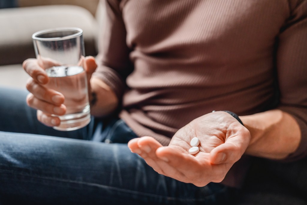 Close-up of a senior man holding two pills in one hand and a glass of water in the other.