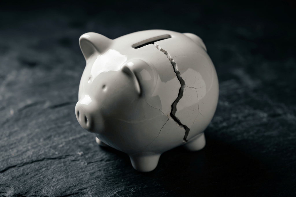 A cracked white piggy bank sits on a dark textured surface.