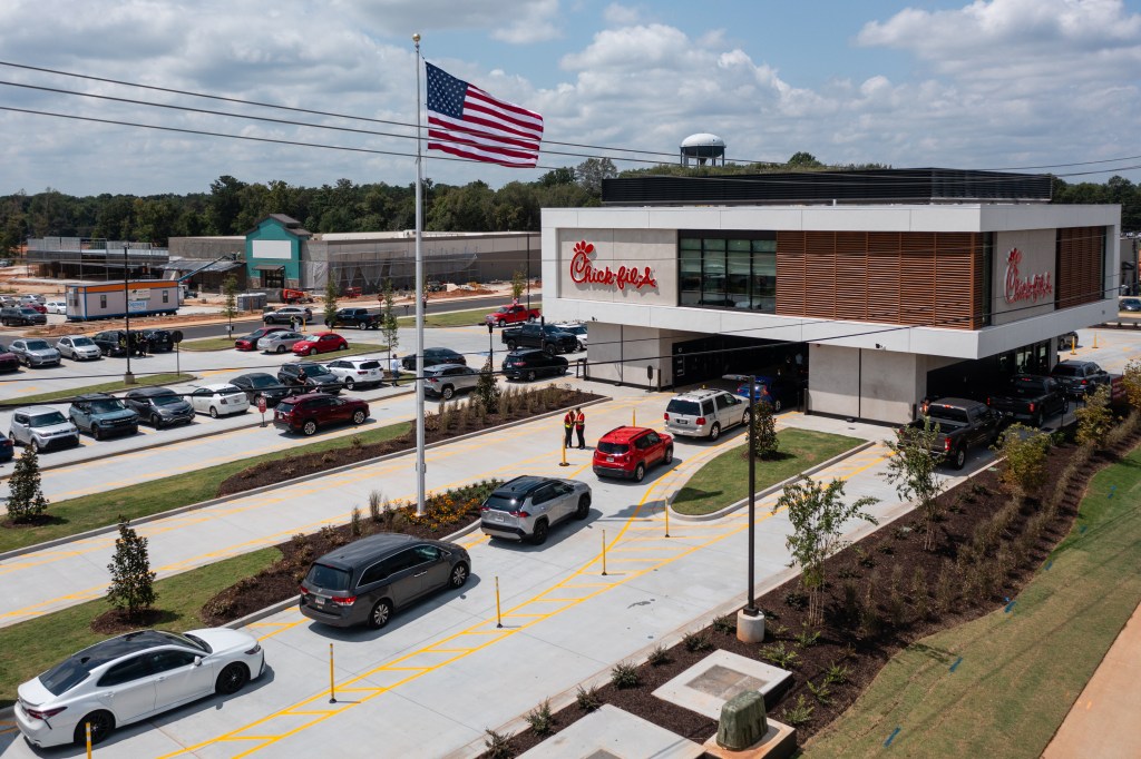 An elevated Chick-fil-A restaurant with a kitchen above four drive-through lanes, featuring cars waiting in line below.