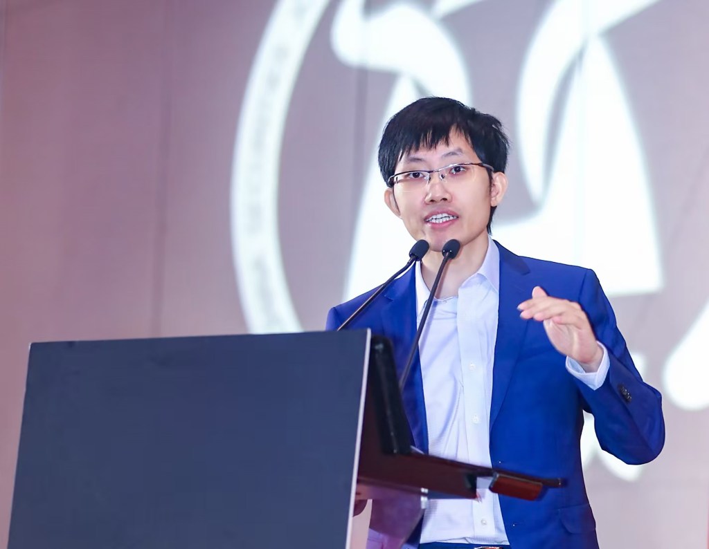 Liang Wenfeng delivering a speech at a podium.