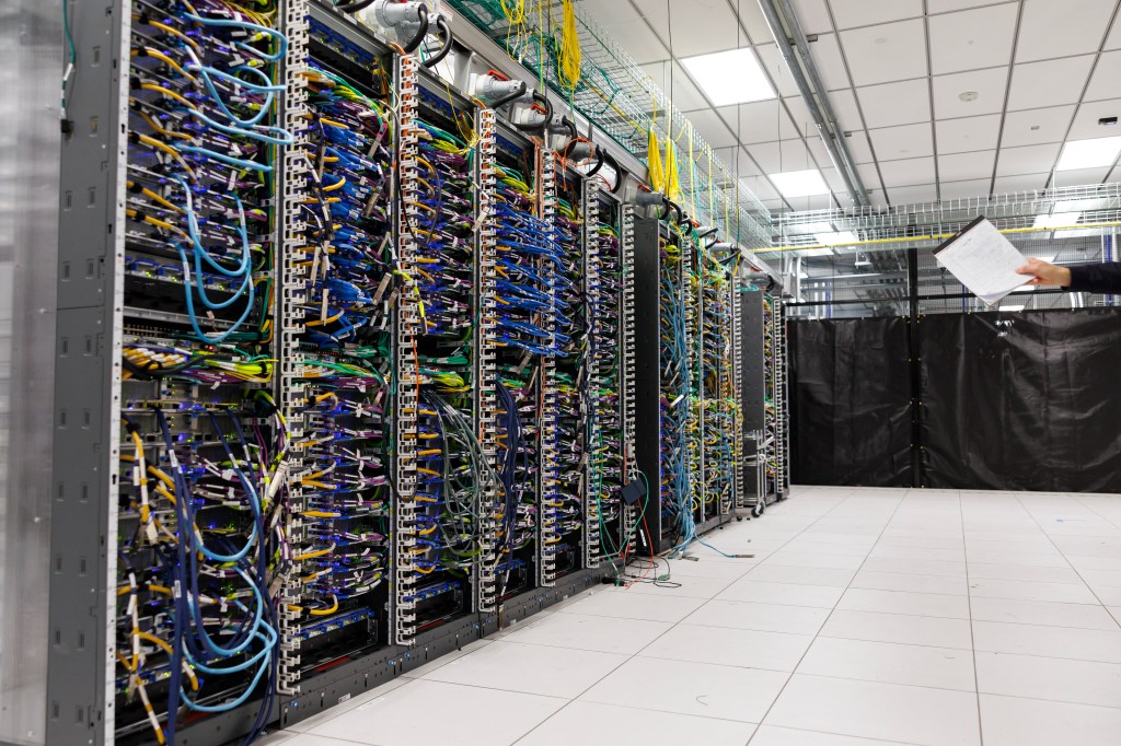 Rows of Amazon Web Services Trainium3 UltraServers with numerous blue and yellow cables are connected in a data lab.