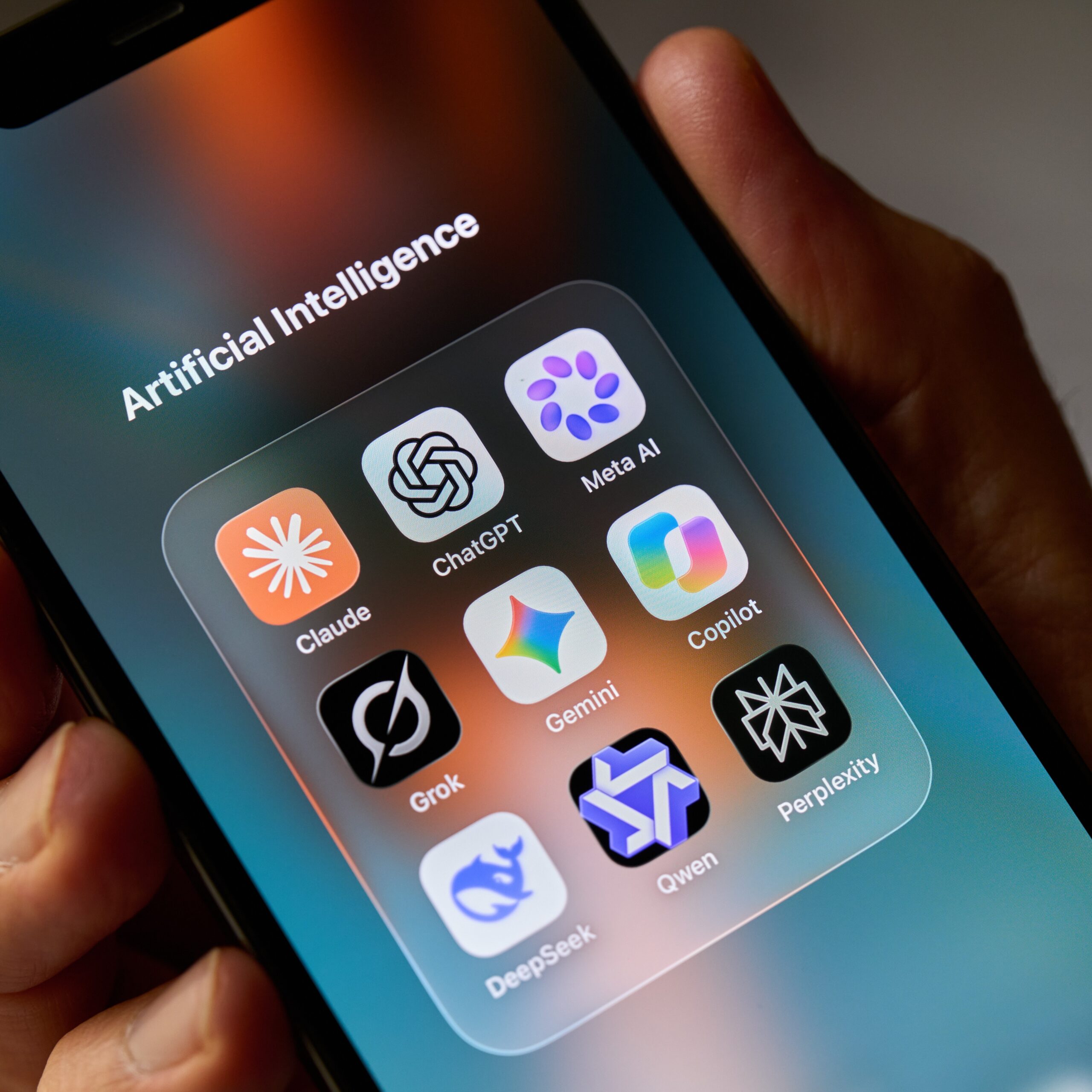 Illustration of a smartphone displaying an "Artificial Intelligence" folder with app icons for Claude, ChatGPT, Meta AI, Gemini, Copilot, Grok, DeepSeek, Qwen, and Perplexity.