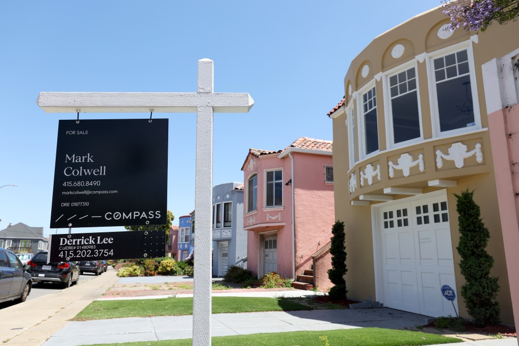 A 'for sale' sign stands in front of a row of colorful homes in San Francisco.
