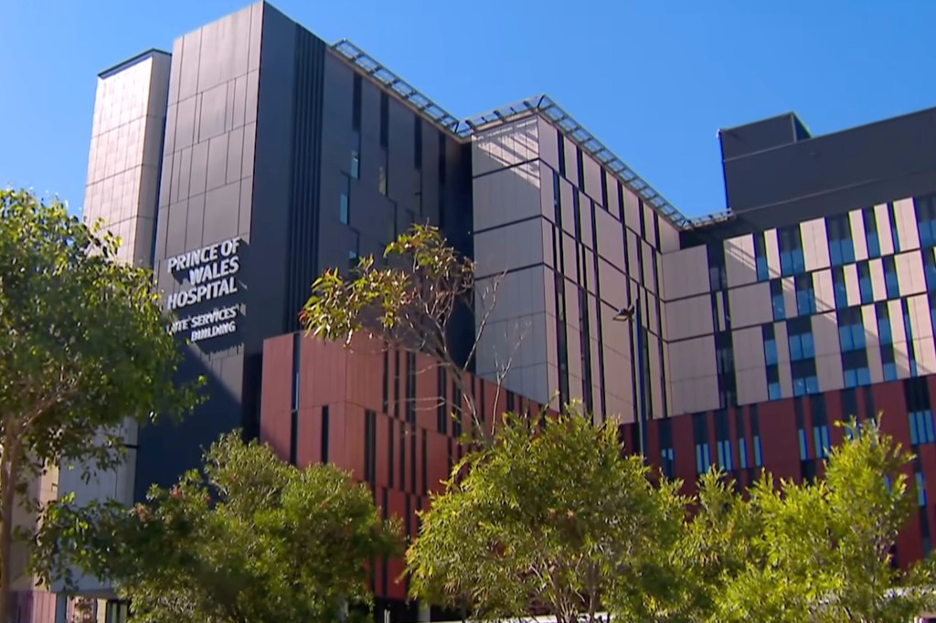 Exterior view of the Prince of Wales Hospital Acute Services Building under a clear blue sky, with trees in the foreground.