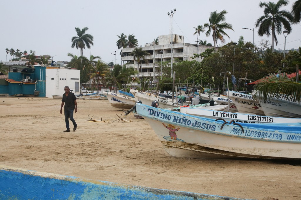A man walks past fishing boats pulled from the sea in Acapulco, Mexico, on Thursday, as Hurricane Trudy moves parallel to Mexico's Pacific coast, threatening more rain and strong winds after recent deadly storms.