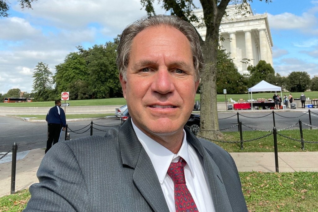 Robert Pfleghardt, 62, posing for an outdoor portrait in front of a monument.