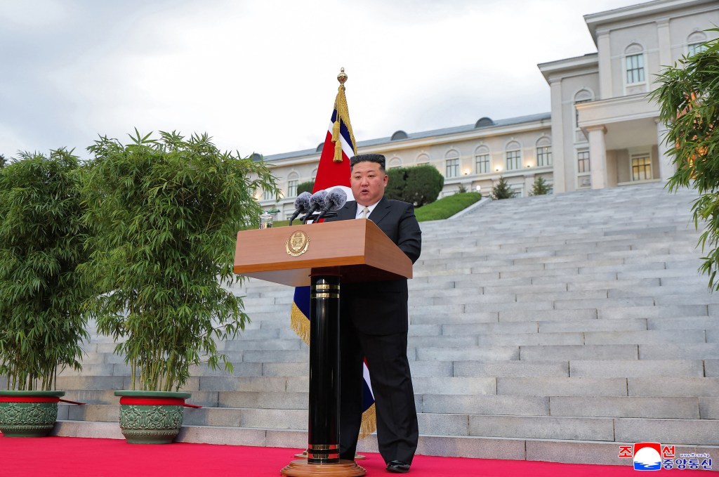 North Korean leader Kim Jong Un delivers a speech at a podium in front of a large building.